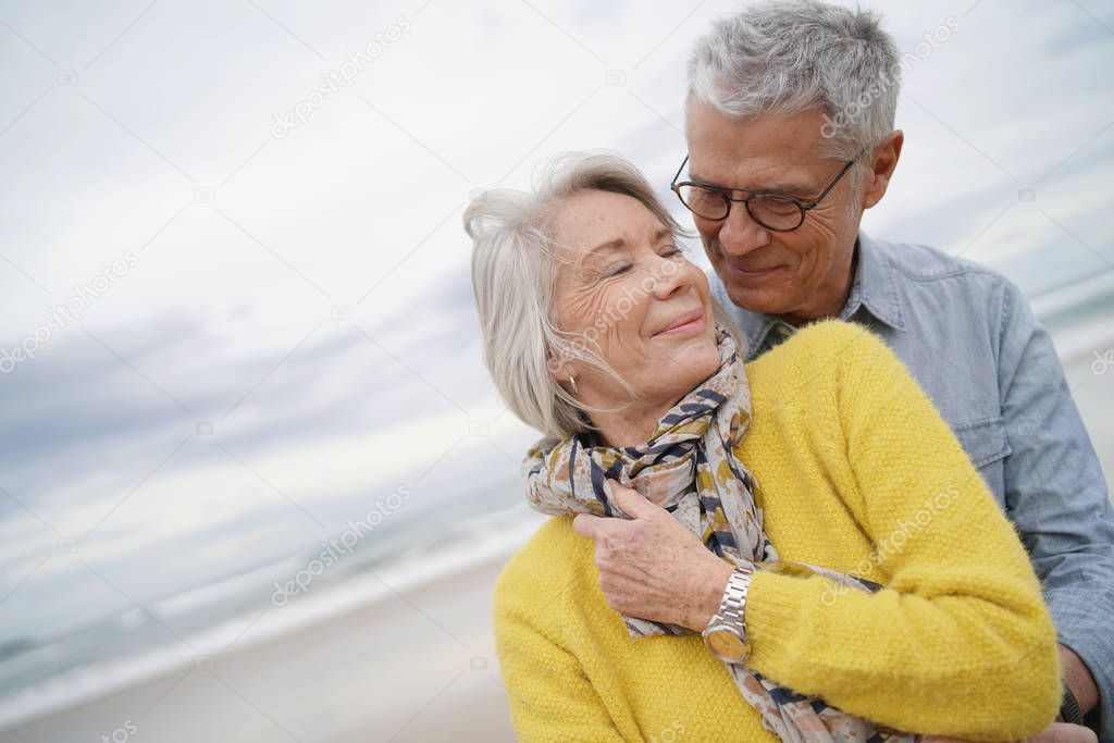 Portrait of attractive vibrant senior couple embracing on beach in fall                              