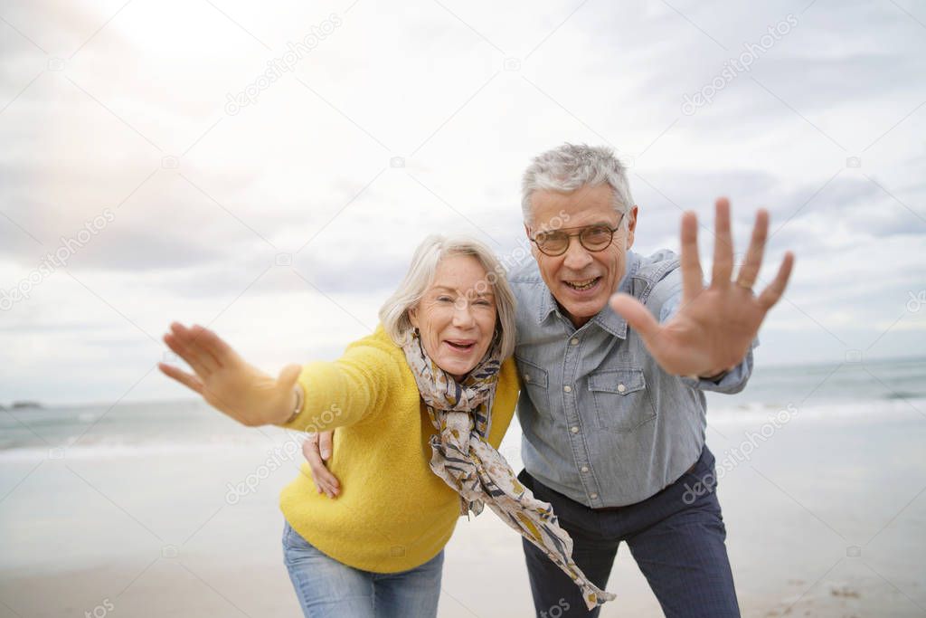  Playful carefree senior couple on beach looking at camera                              