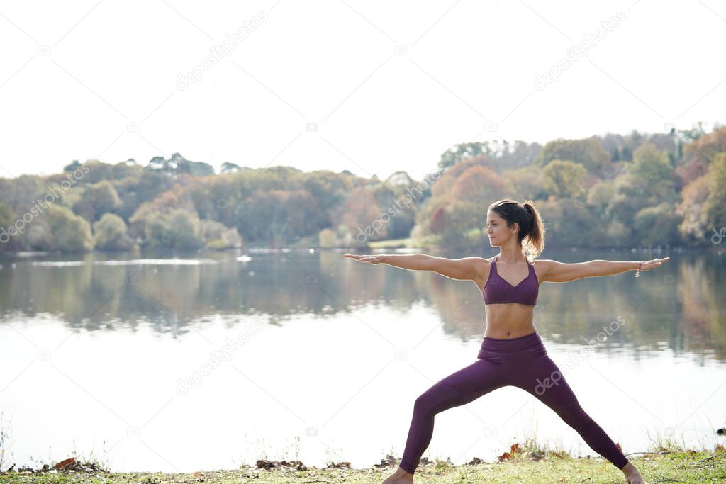 Stunning brunette practicing yoga outdoors by lake in fall