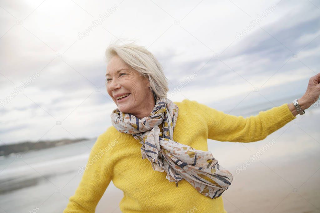  Carefree energetic senior woman playing around on beach in fall                             