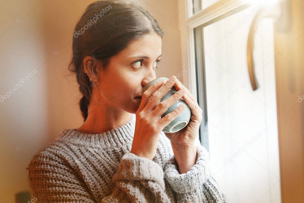 Calm attractive brunette looking out of window with hot drink