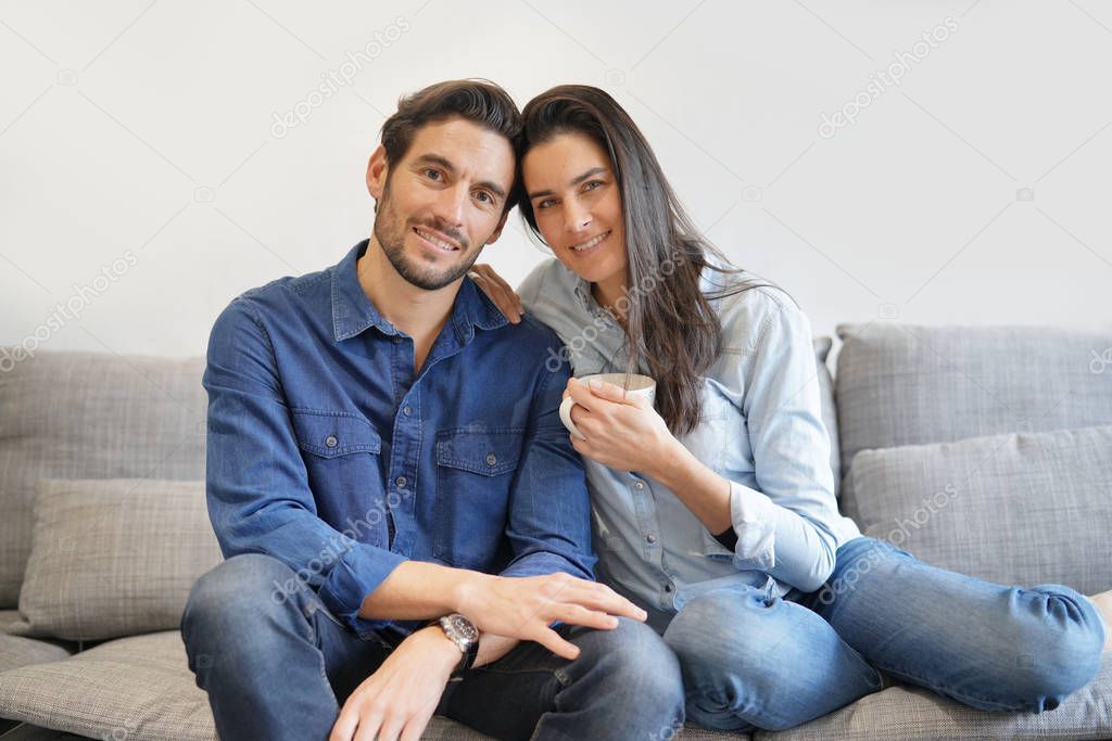 Isolated gorgeous smiling couple in denim on comfy couch