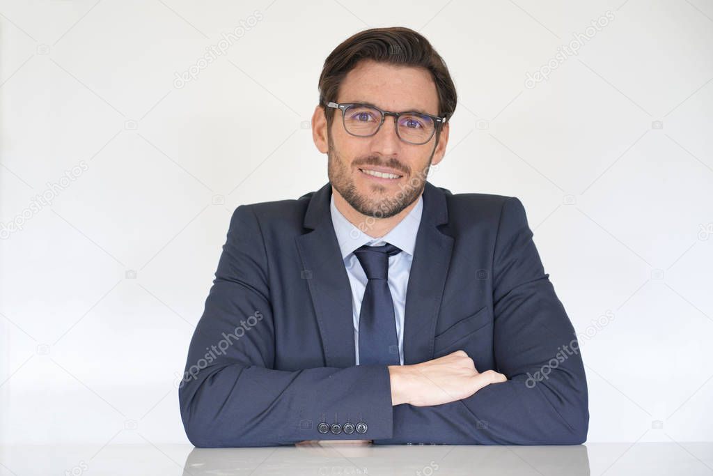Isolated attractive businessman sitting at desk in suit with arms crossed