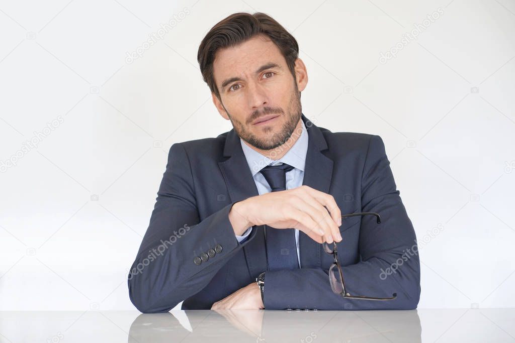 Isolated attractive serious businessman siting at desk in suit