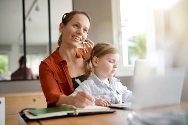 Mother working from home on computer with her young daughter