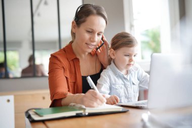 Mother working from home on computer with her young daughter