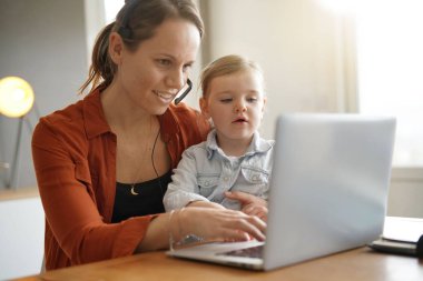 Mother working from home on computer with her young daughter