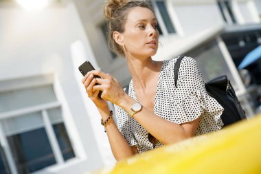 Modern stil genç kadın cep telefonuyla güneşli bir şehirde klasik arabanın yanında.