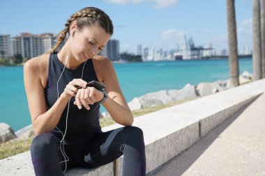 Gülen sportif genç kadın güneşli havada cep telefonu kontrol