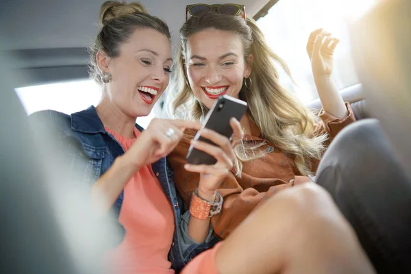 Two attractive friends talking and laughing in casual evening wear in back of taxi