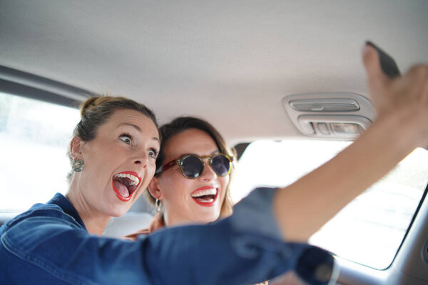 Two attractive friends taking selfie in back of taxi 