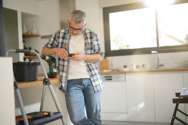 Modern mutfak merdiveninde eğilerek cep telefonu kontrol el işleri ustası