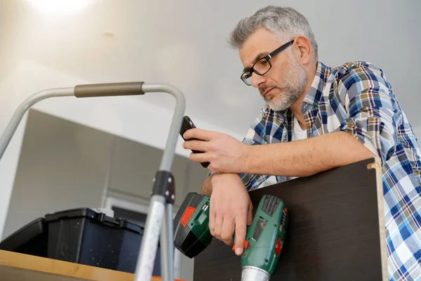 Älterer Mann Checkt Telefon Während Regal Moderner Küche Repariert — Stockfoto