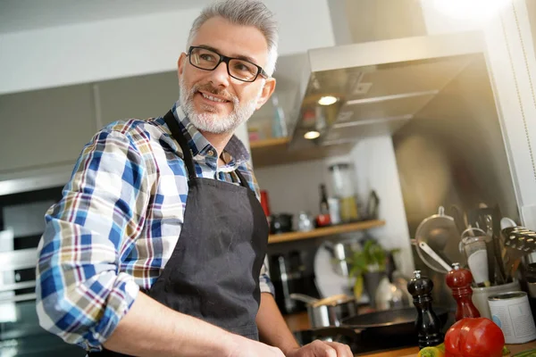 Cheerful mature man in kitchen preparing dish