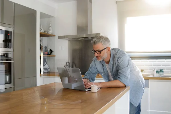 モダンなキッチンに自宅のコンピューターを持つ男 — ストック写真