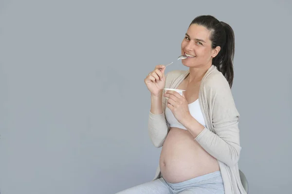 Беременная Женщина Сером Фоне Ест Йогурт — стоковое фото