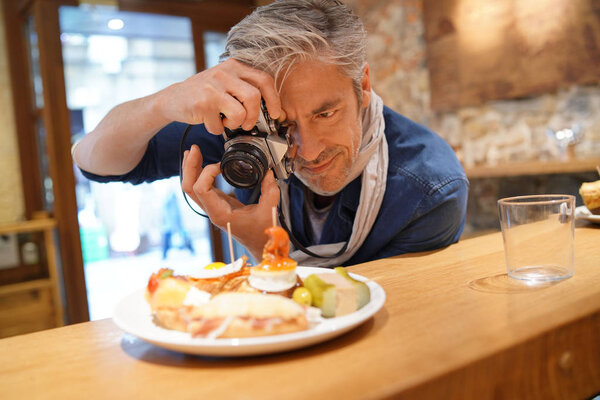 Mature photographer taking photos of tapas plate in Spanish restaurant