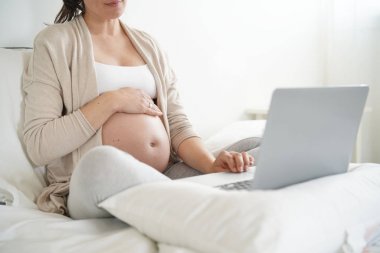 Hamile kadın yatakta rahatlatıcı, dizüstü bilgisayar kullanarak