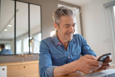 Evden çalışan olgun adam cep telefonuna bakıyor