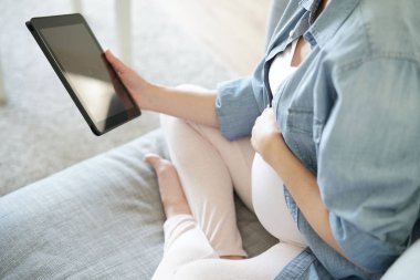 Dijital tablet kullanan hamile kadın, kanepede dinleniyor