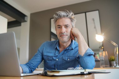 Evden çalışan olgun adam kameraya bakıyor