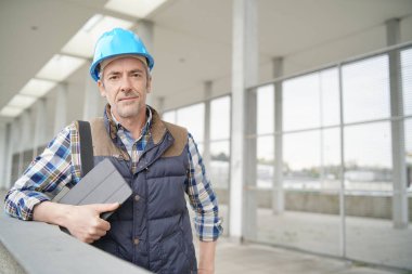 Çağdaş binanın dışında kameraya bakan inşaat işçisi