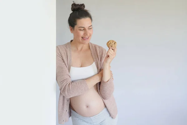Pregnant woman eating a cookie, isolated