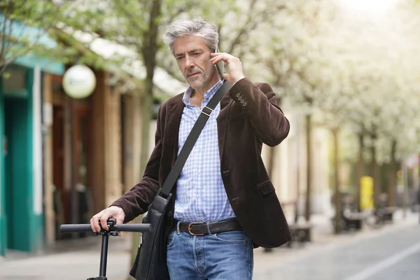Businessman talking on cellphone commuting on micro scooter