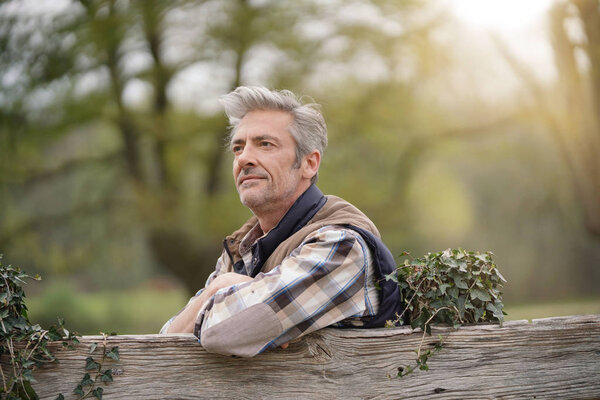 Farmer leaning on fence in field looking out