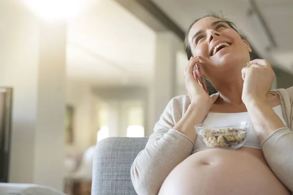 Pregnant woman on the phone, eating cereals