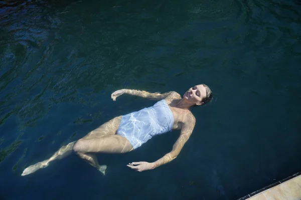 黒いタイル張りのプールで泳ぐエレガントな女性のトップビュー — ストック写真