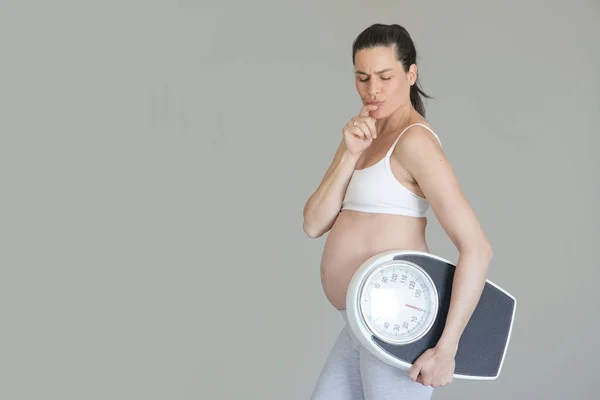 Pregnant woman holding bathroom scale, isolated