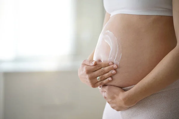 Pregnant woman applying stretch mark removal lotion on her belly
