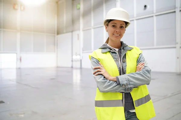 Female construction worker smiling at camera in empty warehouse