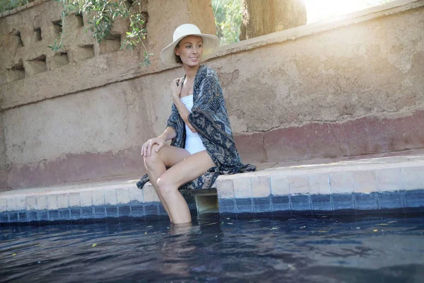 Stunning woman siting by Moroccan swimming pool