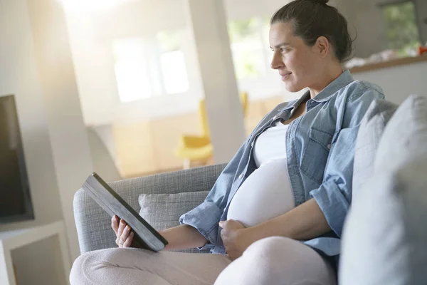 Femeie Gravidă Care Utilizează Tabletă Digitală Relaxându Canapea Imagini stoc fără drepturi de autor