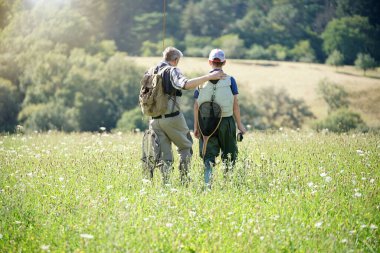 Bir baba ve oğul sinek avından dönüyor ve çayırda yürüyor.
