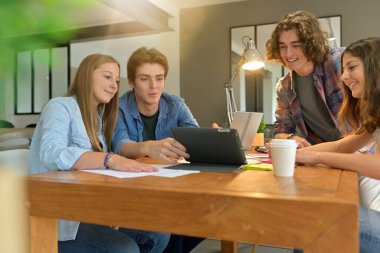 Proje üzerinde çalışmak için masanın etrafında toplanan genç öğrenciler