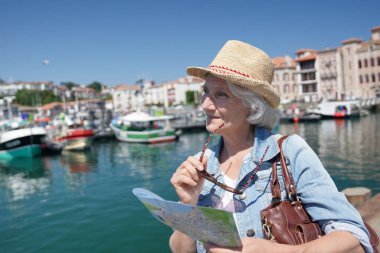 Turistik kenti ziyaret eden şapkalı yaşlı bir kadının portresi. Şehir haritası okuyor.