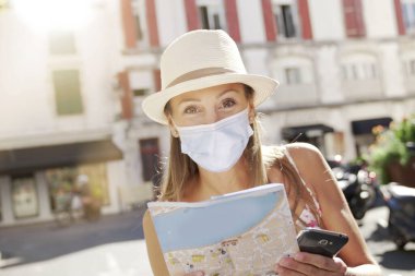 Yüz maskesi olan turist kadın harita okuyor ve akıllı telefon kullanıyor.
