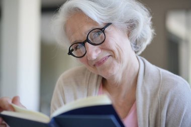 Koltuğunda oturup kitap okuyan kıdemli bir kadın.
