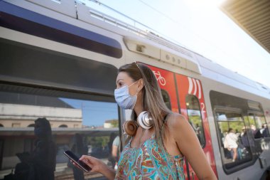 Tren istasyonunda yüz maskesi takmış, tren bekleyen genç bir kadın.