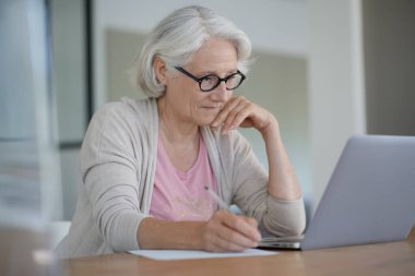 Evde dizüstü bilgisayar kullanan yaşlı bir kadın.