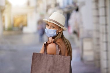 Genç bir kadın turist bölgesinde alışveriş yapıyor, maske takıyor.