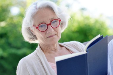 Dışarıda kitap okuyan kıdemli kadın.
