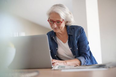 Evde dizüstü bilgisayar kullanan yaşlı bir kadın.