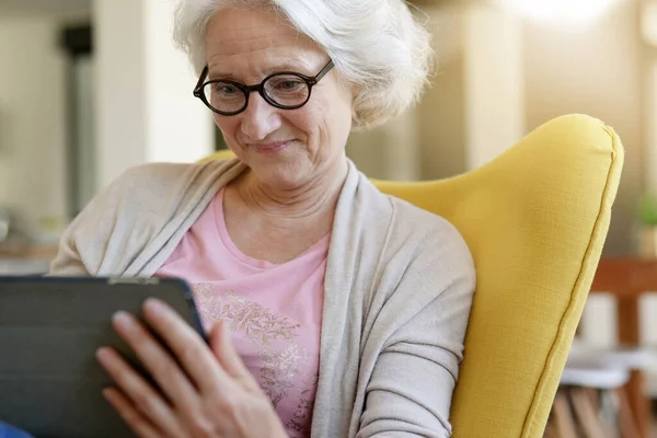 Ηλικιωμένη Γυναίκα Χαλαρώνοντας Στην Πολυθρόνα Και Χρησιμοποιώντας Ψηφιακό Δισκίο — Φωτογραφία Αρχείου