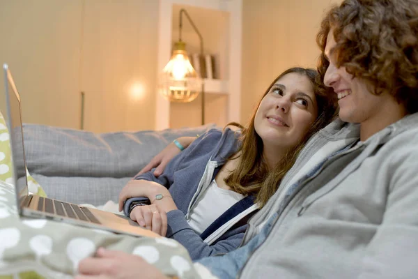 Young couple of students at home watching movie on laptop