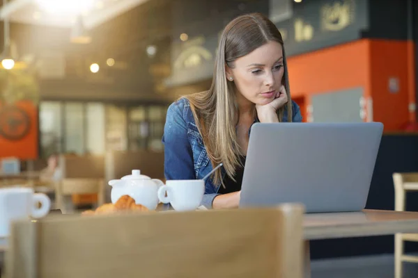 若い女性がコーヒーショップに座ってラップトップで働いています — ストック写真