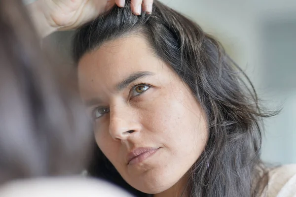 鏡の前で髪の毛の根をチェックする中年女性 — ストック写真